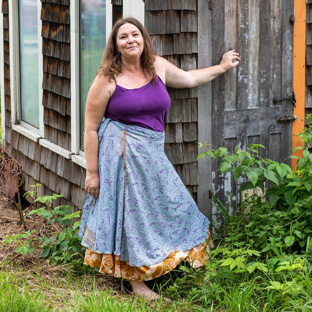 Model is standing outside next to a wooden building wearing a light blue ankle length sari wrap skirt.