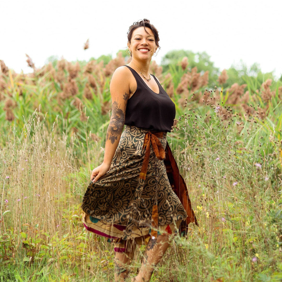 A woman smiling on a field full of grass wearing a sari wrap skirt.