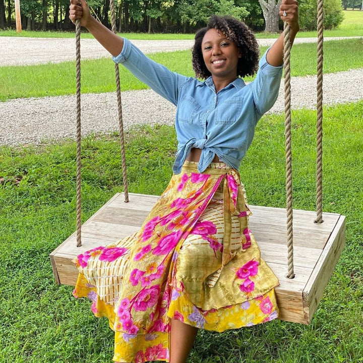 Woman on a wooden swing smiling, with a grass background.