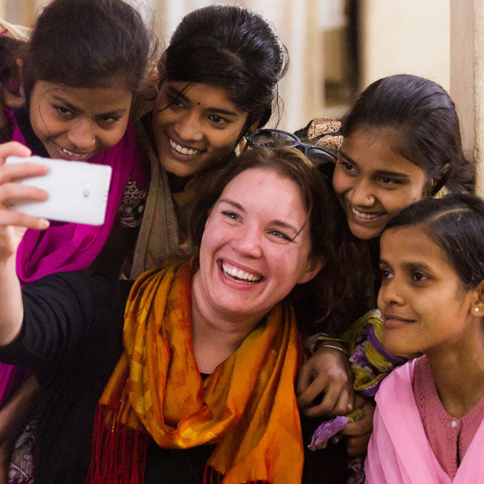 A woman, smiling with four girls, taking a group selfie