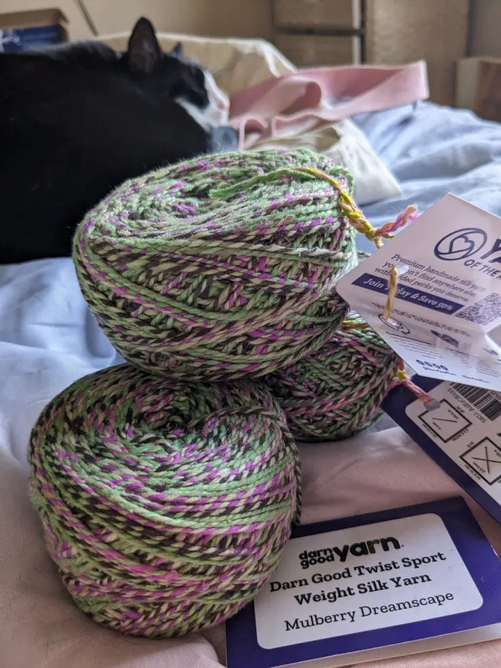 A Yarn balls labeled "Darn Good Yarn," in green, purple, and a black cat in the background